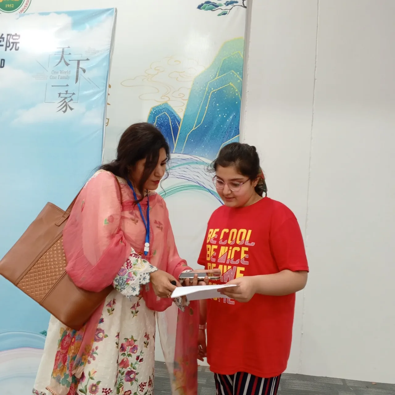 Teacher and Student reviewing paper under Tian Xia Yi Jia calligraphy banner